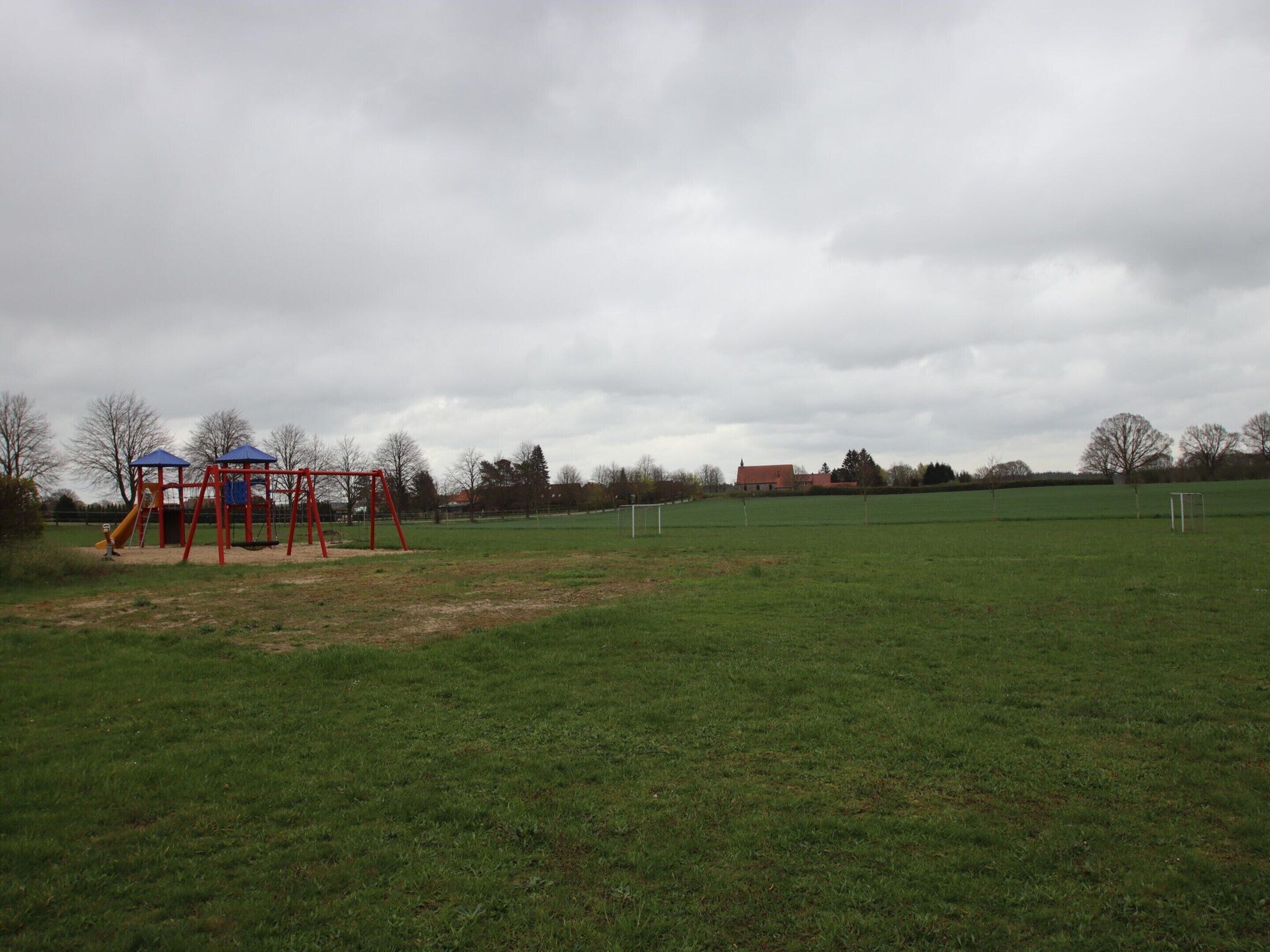 A playground with a swing set and slide, a soccer goal, and a grassy field.
