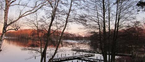 A serene lakeside scene with a wooden pier extending into the water, surrounded by leafless trees and a calm lake reflecting the sky.