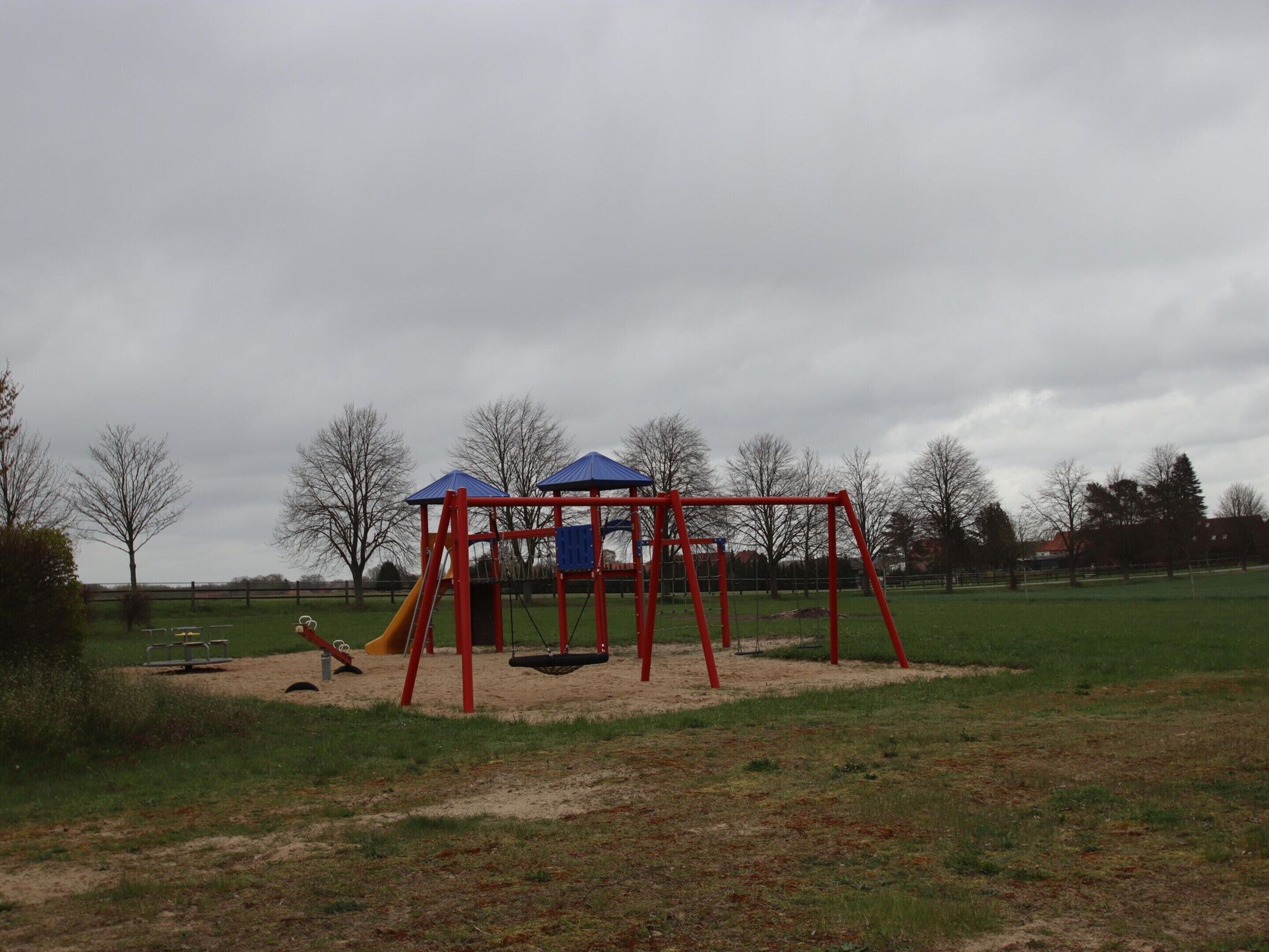 A playground with swings and slides, surrounded by a grassy field and trees.