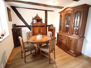 A dining room with a wooden table and chairs, a wooden cabinet with glass doors, and a ceiling with exposed beams. - Ferienhaus in Wittendtsrp OT Pogress (Wittendörp)