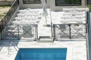 Ein Schwimmbecken mit Fliesen umrandet, weißen Liegestühlen und einer Metalltreppe.
