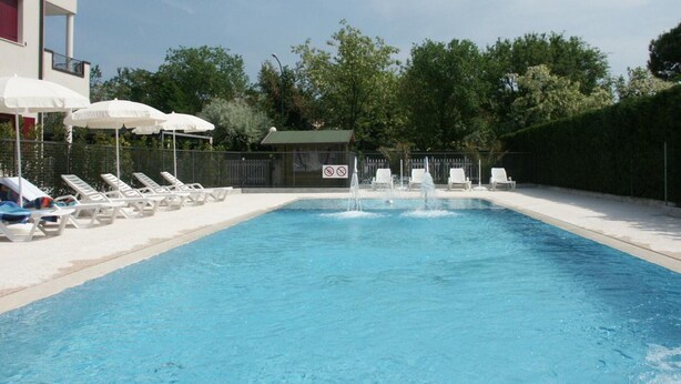 Ein Swimmingpool mit Liegestühlen und Sonnenschirmen, umgeben von einem Zaun und Bäumen.