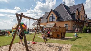 En legeplads med gynger og et klatrestativ, et stort hus med et stejlt tag, og et grønt græsområde.