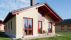 Et moderne hus med rødt tag, store vinduer og en lille terrasse.