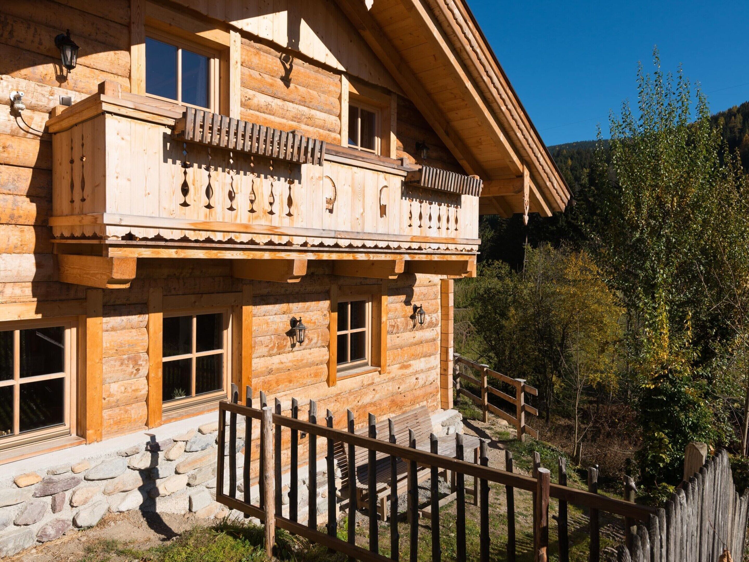 Un chalet en bois doté d’un balcon, de fondations en pierre et d’une clôture en bois.