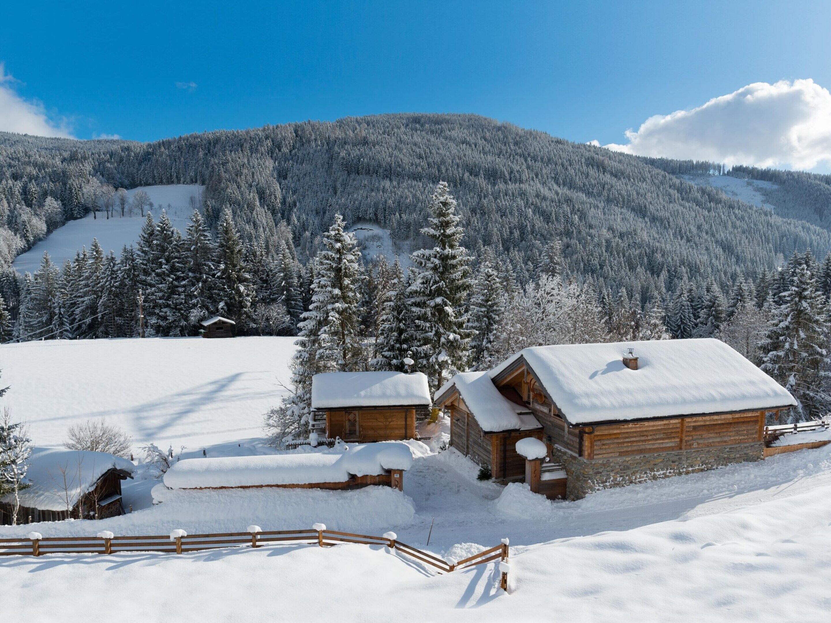 Un albergue cubierto de nieve con fachada de madera, frente a un paisaje de árboles cargados de nieve y una montaña.