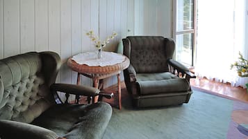 Una habitación con dos sillones tapizados, una mesita redonda con mantel de encaje y un ventanal con vistas al exterior.