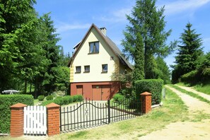 Une maison à deux étages avec un toit brun, des murs de couleur beige et une clôture blanche en bois.