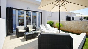 A modern outdoor patio with wicker furniture, a large umbrella, and a stone wall. - Apartments in Villas Punta Skala With Beachpool (Zadar)