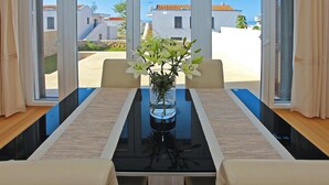A dining table with a vase of flowers, two chairs, and a view of buildings through large windows. - Apartments in Villas Punta Skala With Beachpool (Zadar)
