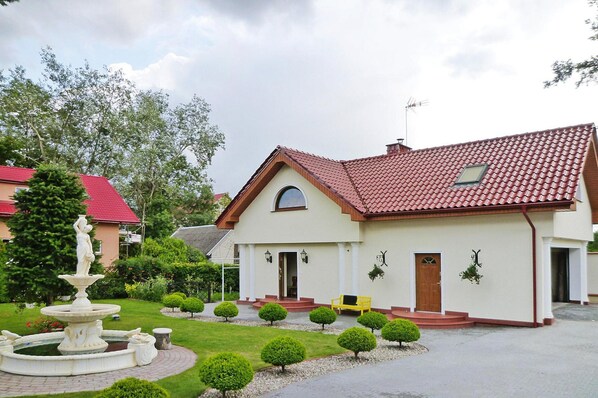 A two-story house with a red-tiled roof, a front garden with a fountain, and a bench. - Holiday Home Sobieszewo Near Baltic Sea (Gdańsk)