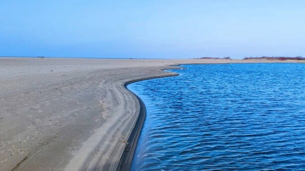 Una playa con cielo azul despejado y agua tranquila.