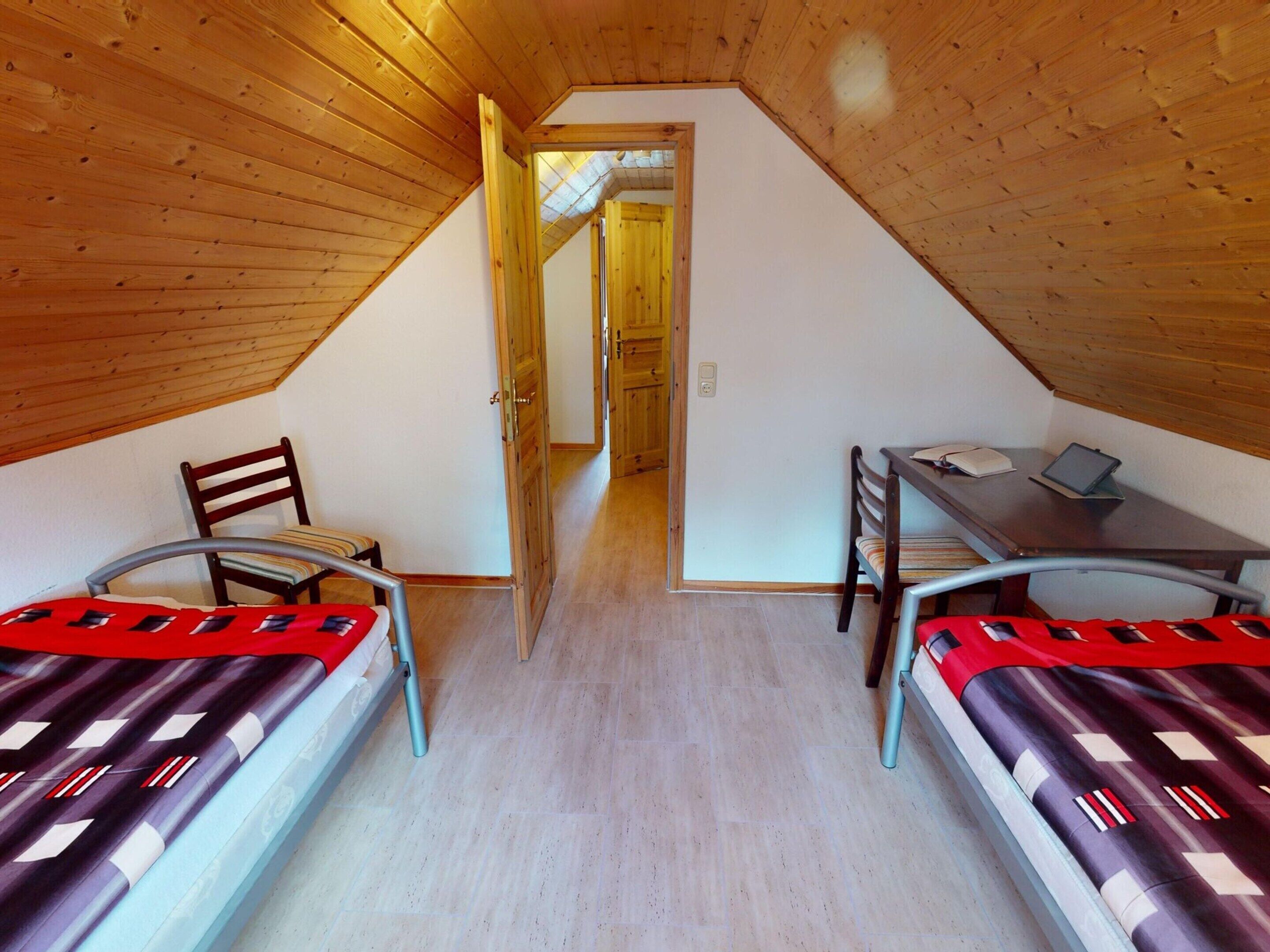 A small, cozy attic bedroom with two single beds, a desk, and a chair.