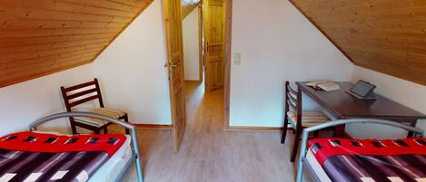 A small, cozy attic bedroom with two single beds, a desk, and a chair.