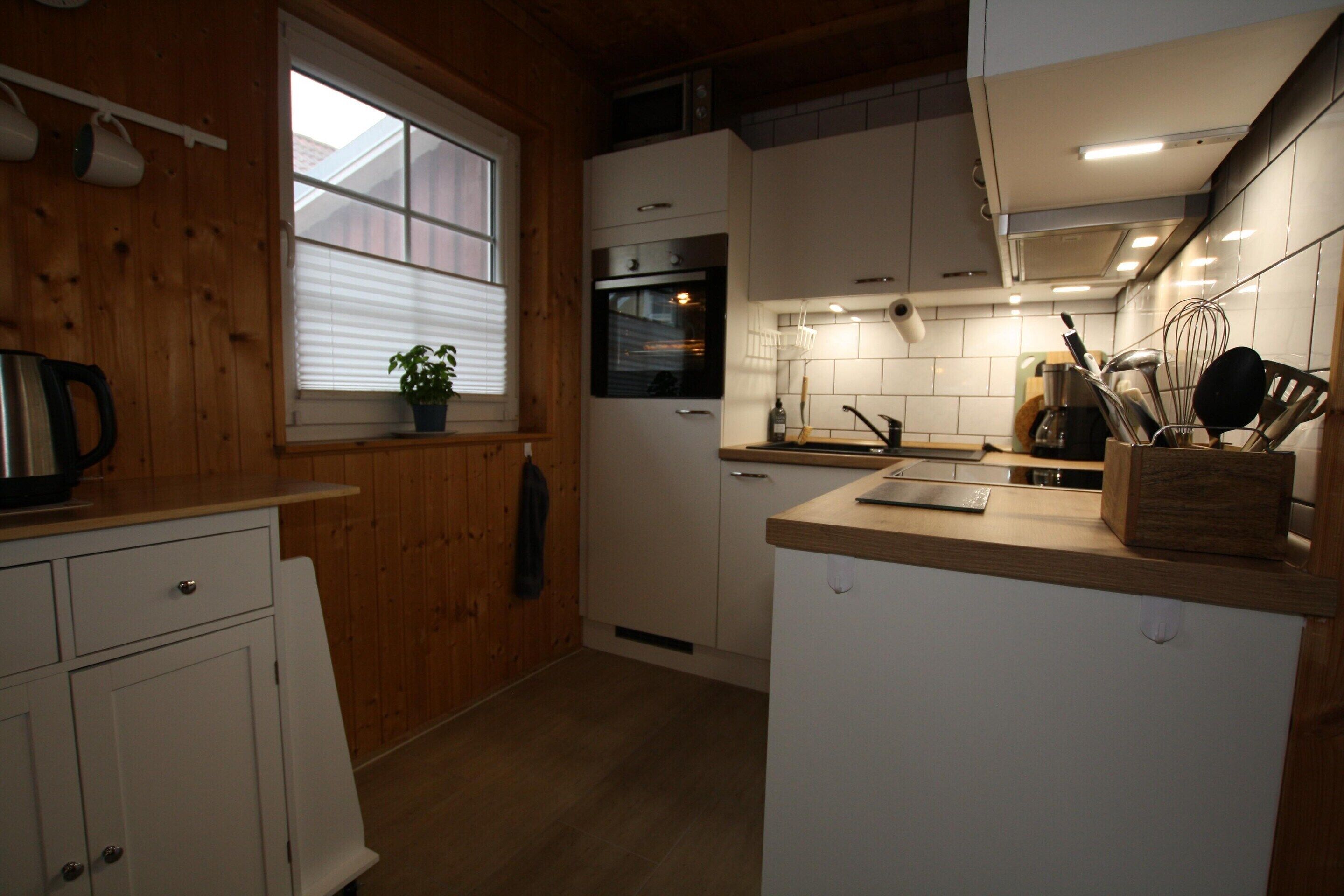A compact kitchen with wooden walls, a built-in oven, and white cabinets.