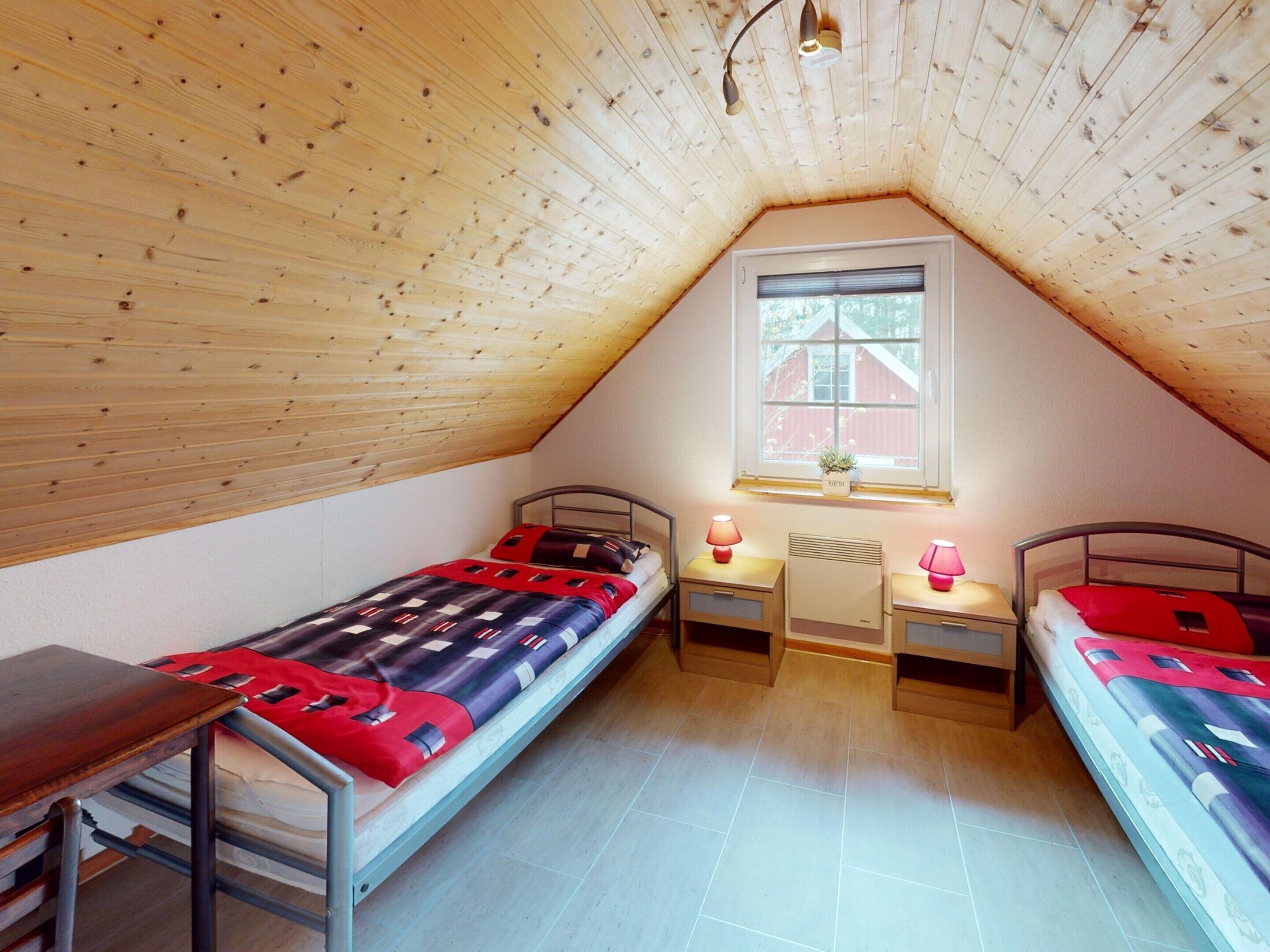 Ein kleines, gemütliches Schlafzimmer im Dachgeschoss mit zwei Einzelbetten, einem Fenster mit Ausblick und einer Holzbalkendecke.
