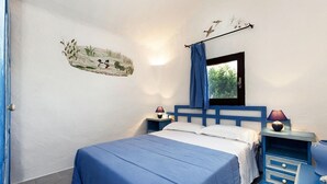 A bedroom with a bed, two bedside tables, a nightstand, a window with a view of trees, and a wall mural. - Holiday Home I Cormorani in Baja Sardinia (Arzachena)