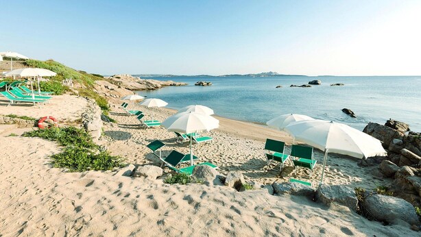 A beach with green lounge chairs and white umbrellas, rocky shoreline, and calm sea. - Holiday Home I Cormorani in Baja Sardinia (Arzachena)