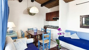 A compact living space with a dining area, kitchenette, and a sofa with striped cushions. - Holiday Home I Cormorani in Baja Sardinia (Arzachena)