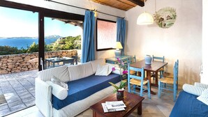A cozy room with a sofa, dining table, chairs, and a view of the sea. - Holiday Home I Cormorani in Baja Sardinia (Arzachena)