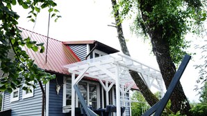 A house with a porch, a metal roof, and a large tree. - Holiday Home Near Lake Mausz With Sauna (Parchowo)