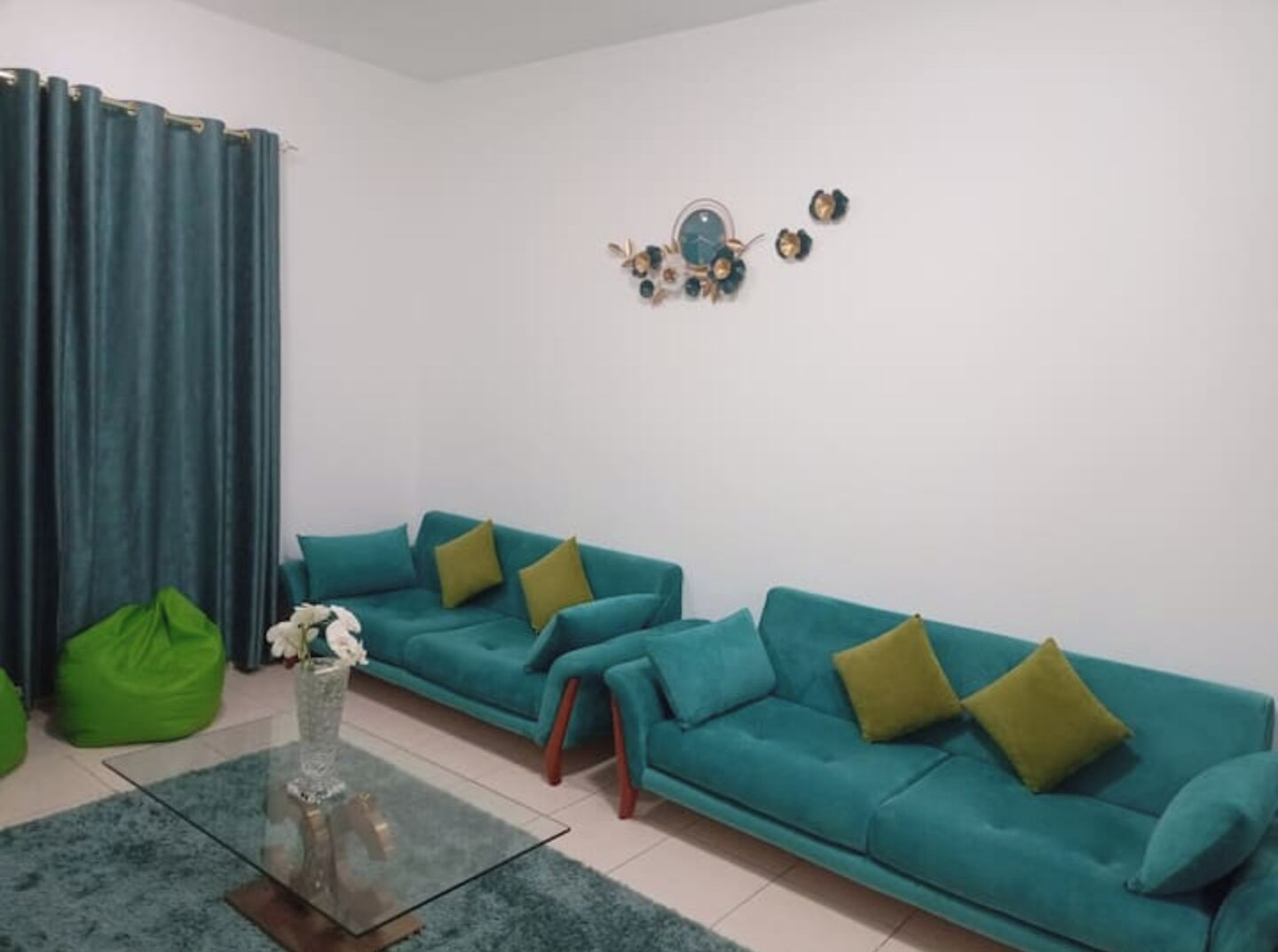 A living room with teal sofas, green cushions, a glass coffee table, and a green bean bag.