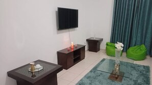 Een moderne woonkamer met een flatscreen televisie aan de muur, een donker houten bijzettafeltje met een lamp en een groene relaxfauteuil.