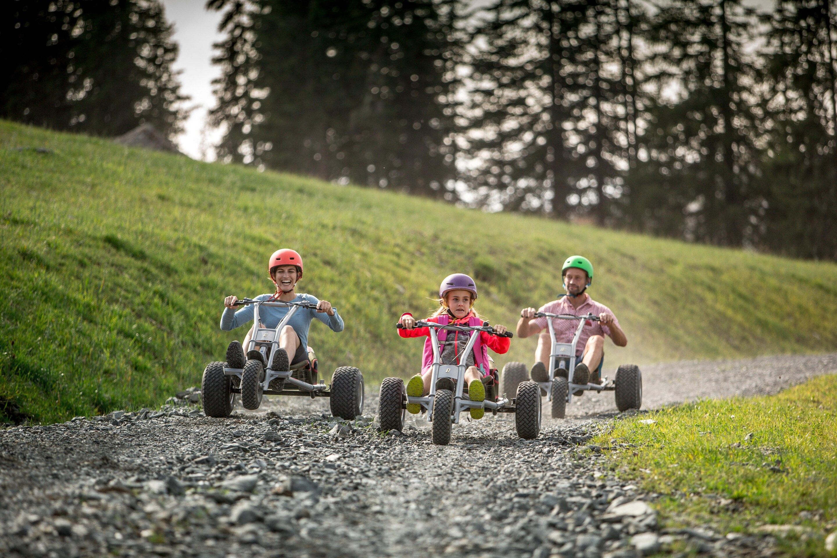 Three individuals on all-terrain vehicles on a gravel path surrounded by grass and trees.