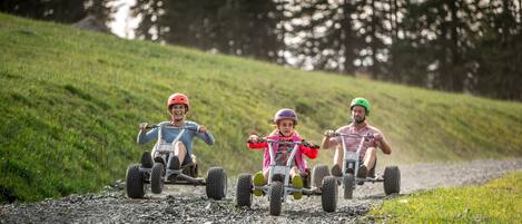 Three individuals on all-terrain vehicles on a gravel path surrounded by grass and trees.