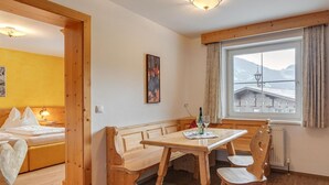 A cozy room with a wooden bed, a bench, a table with chairs, and a window with a view of mountains. - Apartment in Fugen Near Spieljoch Ski Lift (Fuegen)