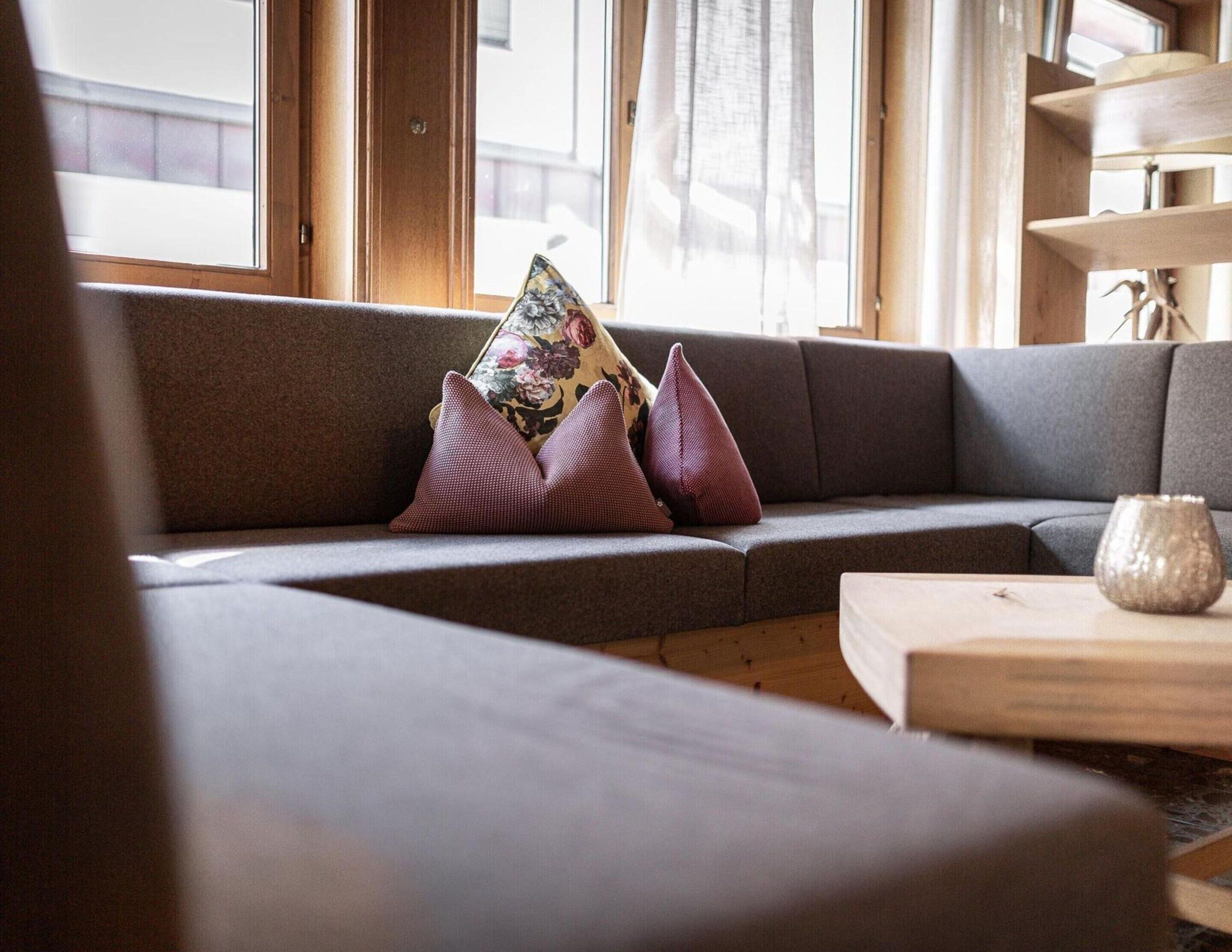 A modern living room with a grey sofa, two patterned cushions, and a wooden coffee table.