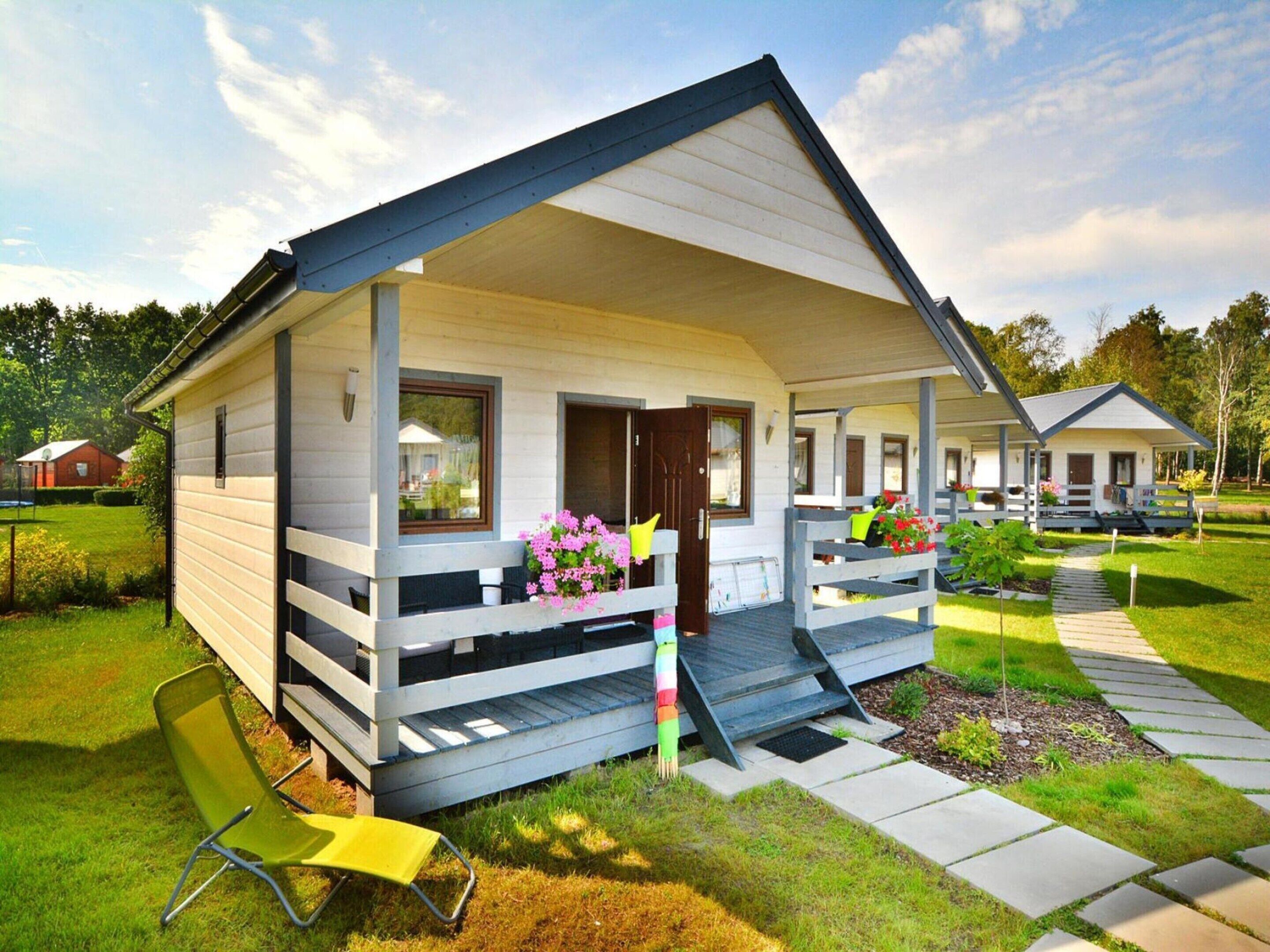 A single-story mobile home with a porch, a small garden, and a pathway leading to the entrance.