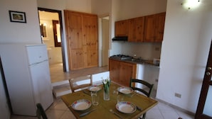 A dining area with a wooden table set for two, surrounded by chairs. A refrigerator is visible to the left, and wooden cabinets are in the background. - Terraced House With Communal Pool Costa Paradiso-formerly TUI Ferienhaus (Trinità d'Agultu e Vignola)