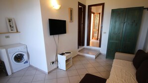 A compact living space with a washing machine, a flat-screen TV mounted on the wall, a sofa, and a green door. - Terraced House With Communal Pool Costa Paradiso-formerly TUI Ferienhaus (Trinità d'Agultu e Vignola)