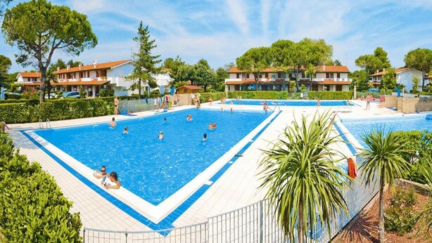 A large outdoor swimming pool surrounded by residential buildings, with clear skies and greenery. - Residence Villaggio Danubio, Bibione Spiaggia (San Michele al Tagliamento)