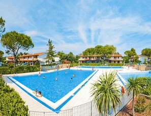 A large outdoor swimming pool surrounded by residential buildings, with clear skies and greenery. - Residence Villaggio Danubio, Bibione Spiaggia (San Michele al Tagliamento)