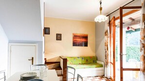 A room with a checkered floor, a table with plates and glasses, a green sofa, a painting on the wall, and a door leading outside. - Residence Villaggio Danubio, Bibione Spiaggia (San Michele al Tagliamento)