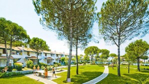 A well-maintained outdoor area with a paved walkway, lush green grass, and mature trees. - Residence Villaggio Danubio, Bibione Spiaggia (San Michele al Tagliamento)