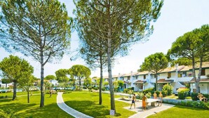 A residential area with a paved pathway, green lawns, and trees. - Residence Villaggio Danubio, Bibione Spiaggia (San Michele al Tagliamento)