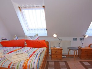A bedroom with a bed, two bedside tables, a desk, a chair, and a radiator. - Appartementhaus Kranichblick, Breege (Breege)