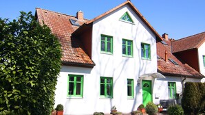 A two-story house with a white facade and green window frames, a red-tiled roof, and a green door. - Appartementhaus Kranichblick, Breege (Breege)