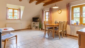 A cozy dining area with a wooden table and chairs, a television on a stand, and a clock on the wall. - Landhaus in Vollerwiek (Vollerwiek)