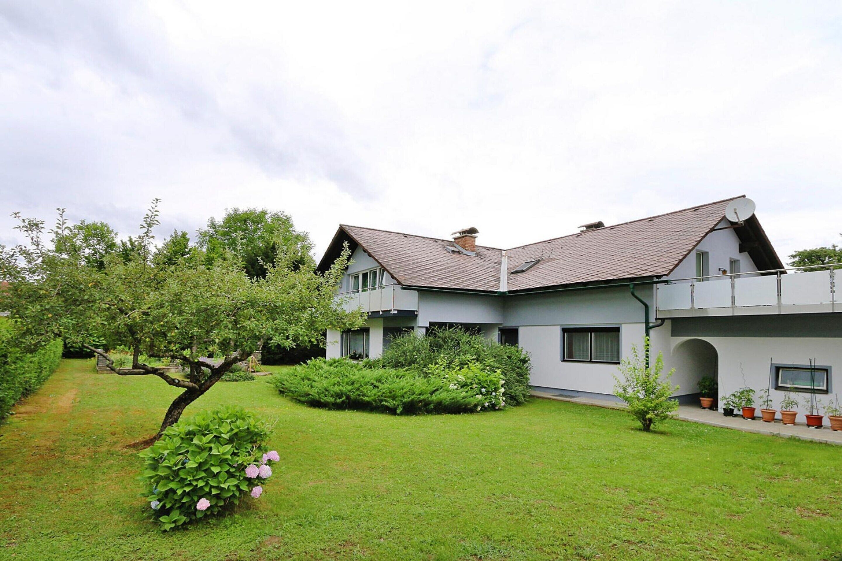 A modern two-story house with a sloped roof, surrounded by a well-maintained garden with various plants and a small tree.