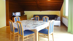 A dining area with a wooden table and chairs, a sofa, and a television in the background. - Apartment in St. Kanzian Near Klopeiner See (Sankt Kanzian am Klopeiner See)