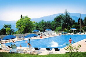 Piscina com espreguiçadeiras e guarda-sóis, rodeada por vegetação e montanhas ao fundo.