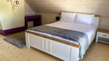 A bedroom with a wooden sloped ceiling, a bed with white bedding, a purple dresser, and a small wooden nightstand.
