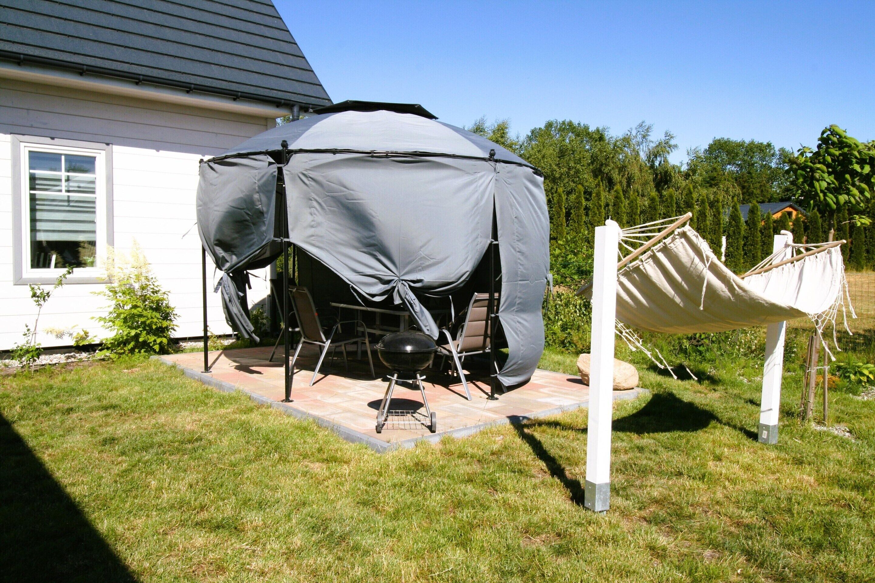 A covered outdoor grill area with a table and chairs, a hammock, and a house in the background.