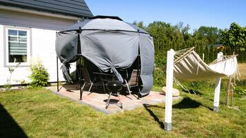A covered outdoor grill area with a table and chairs, a hammock, and a house in the background.