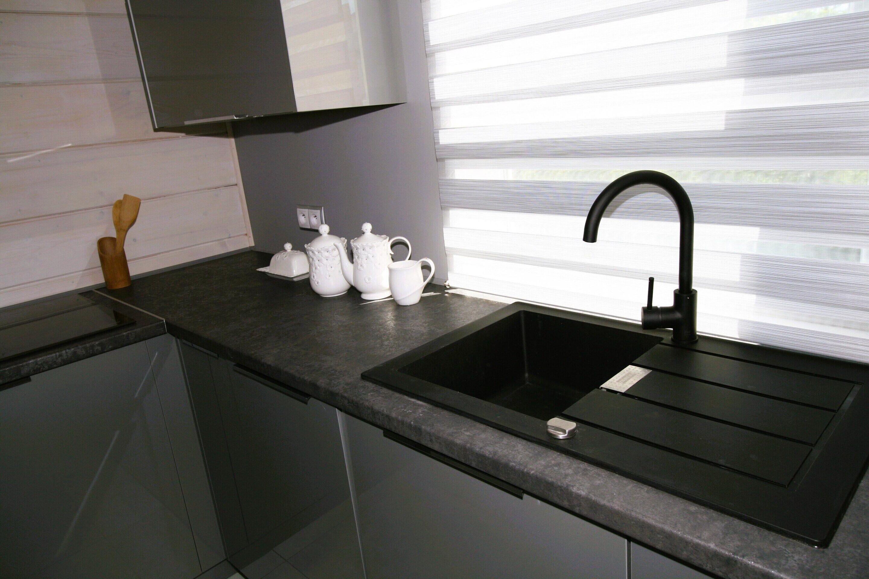 A modern kitchen with a black sink, white teapots, and a wooden spatula on the counter.