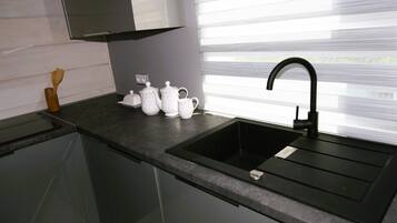 Eine moderne Küche mit einem schwarzen Spülbecken, weißen Teekannen und einem Holzspatel auf der Arbeitsfläche.